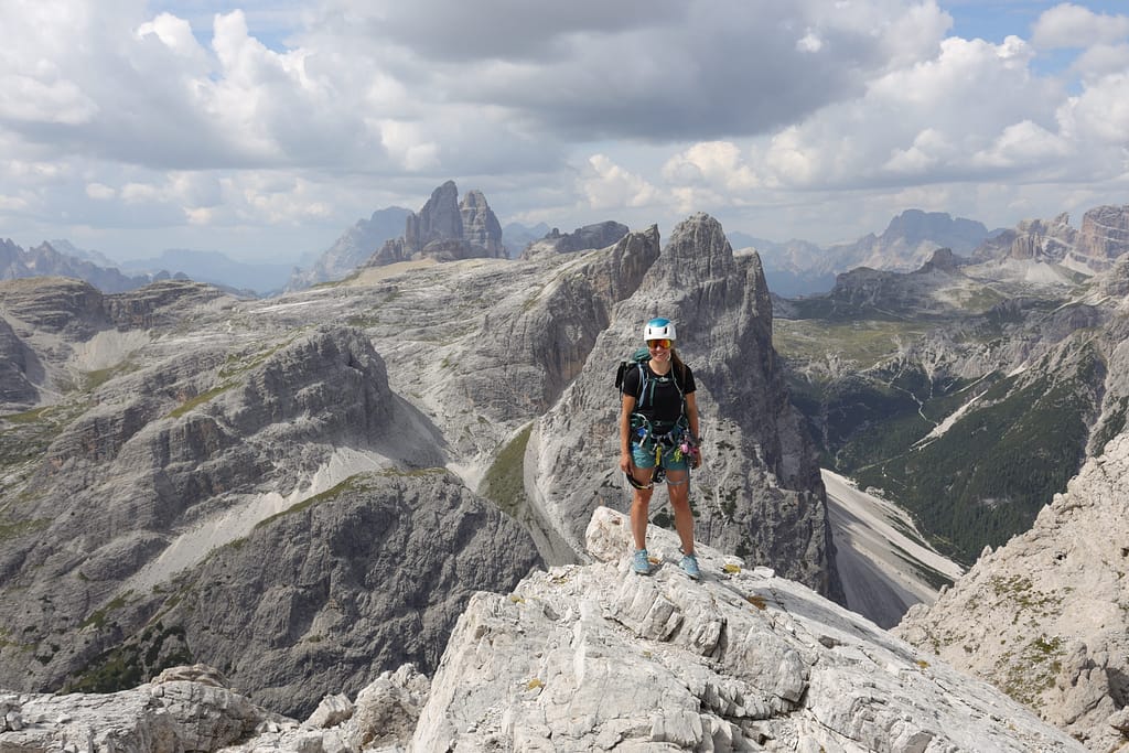 Woman with via ferrata gear standing in front of panoramic views of Italian Dolomites