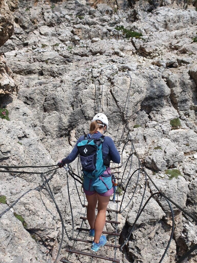 Moteris su via ferrata įranga eina Via Ferrata Cesare Piazzetta esančiu kabančiu tiltu